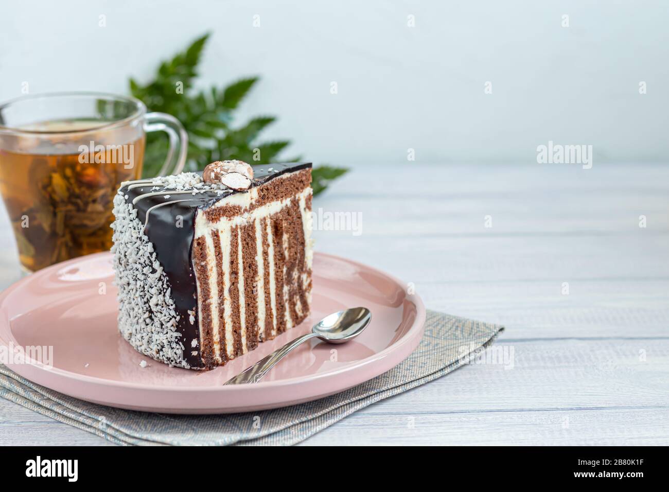 Une tranche de gâteau zébré avec glaçage au chocolat. Sur fond clair. À l'arrière-plan se trouve une tasse de thé floral. Espace de copie Banque D'Images