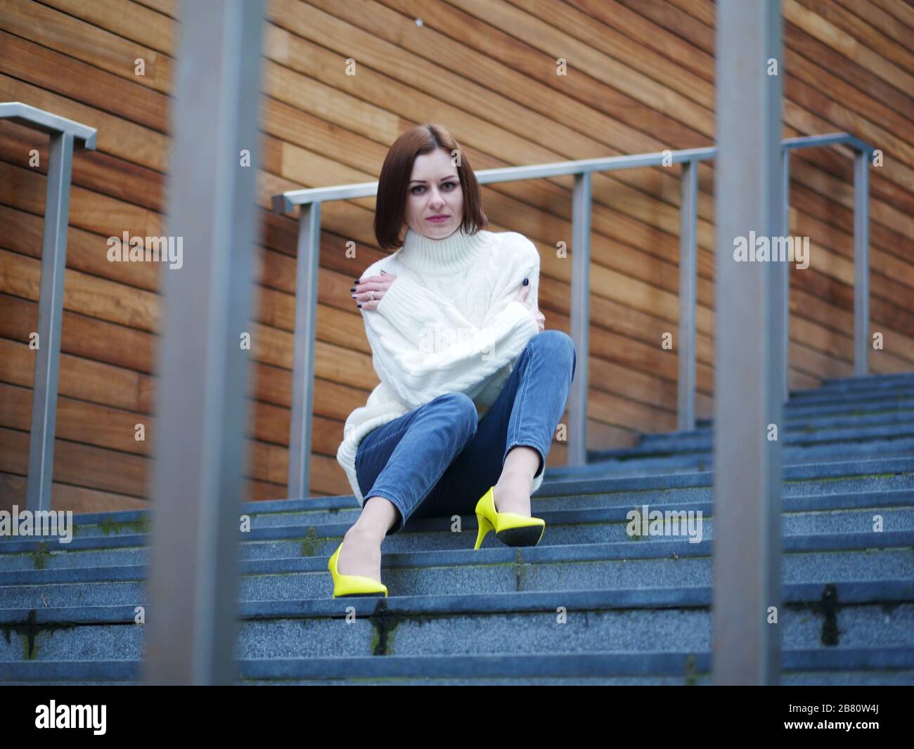 Image d'une belle femme élégante en chaussures jaunes assise sur les escaliers de rue avec des mains croisées. Fond en bois. Banque D'Images