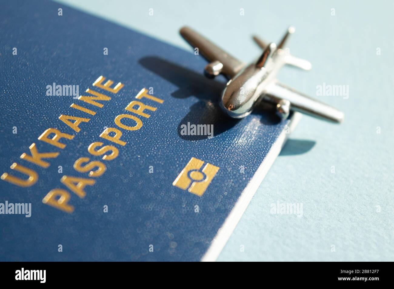 Passeport étranger ukrainien avec figurine métallique de petit avion sur fond bleu clair ensoleillé. Photo conceptuelle tendance de voyage et d'aviation Banque D'Images
