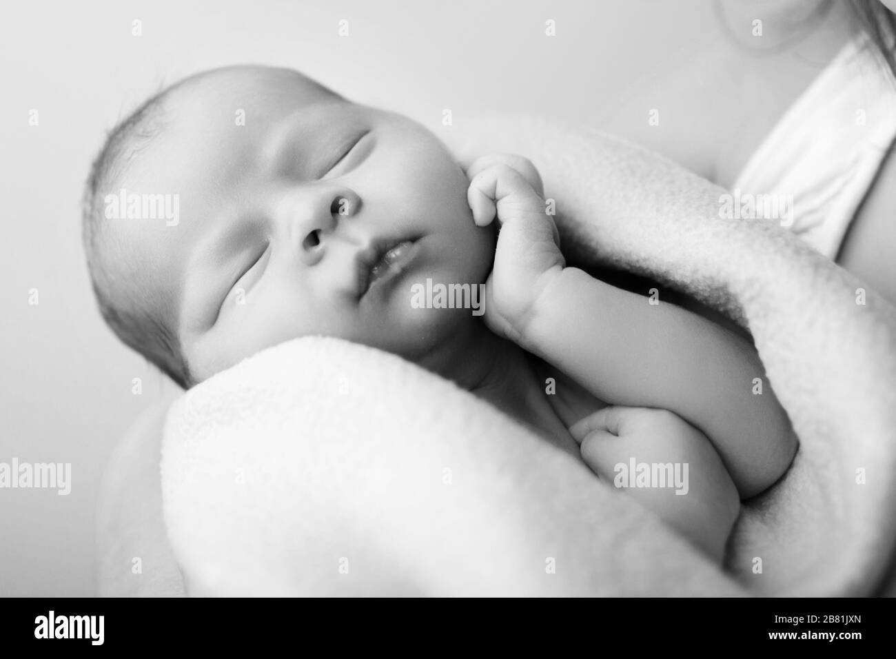 Gros plan bébé nouveau-né mignon enveloppé dans une couverture prenant la sieste. Photo noire et blanche d'un enfant doux touchant le menton au repos sur la petite main pendant le sommeil. Concept Banque D'Images