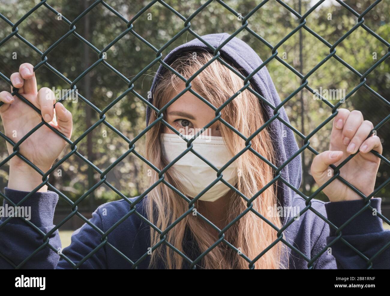 Bordure fermée. Quarantaine. Une jeune femme portant un masque de protection se trouve derrière la bordure de clôture. COVID-19 virus de la pandémie d'infection du coronavirus. Banque D'Images