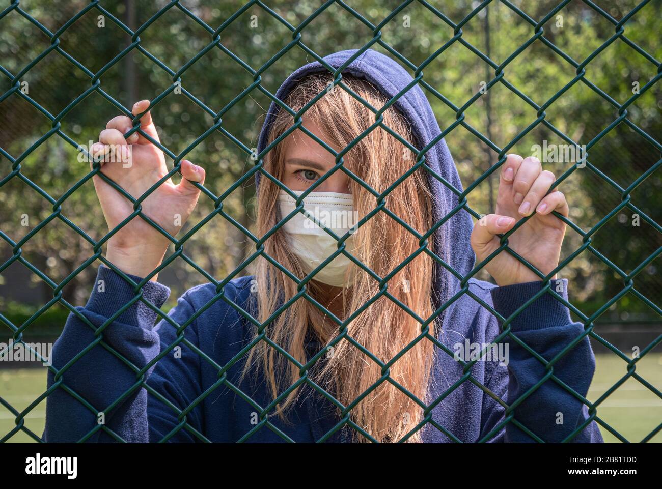 Bordure fermée. Quarantaine. Une jeune femme portant un masque de protection se trouve derrière la bordure de clôture. COVID-19 virus de la pandémie d'infection du coronavirus. Banque D'Images