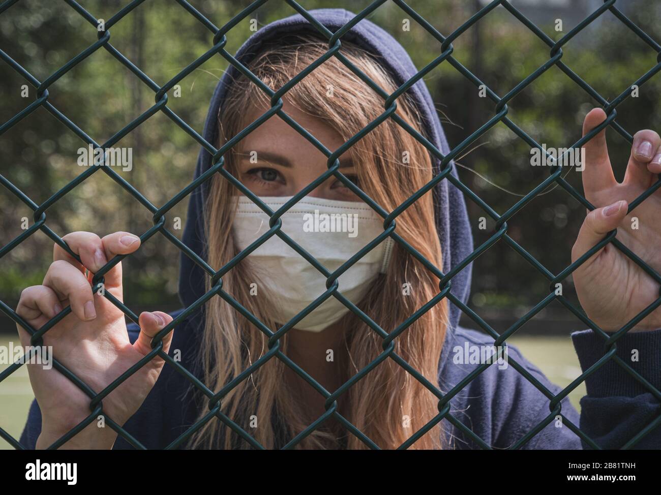 Bordure fermée. Quarantaine. Une jeune femme portant un masque de protection se trouve derrière la bordure de clôture. COVID-19 virus de la pandémie d'infection du coronavirus. Banque D'Images