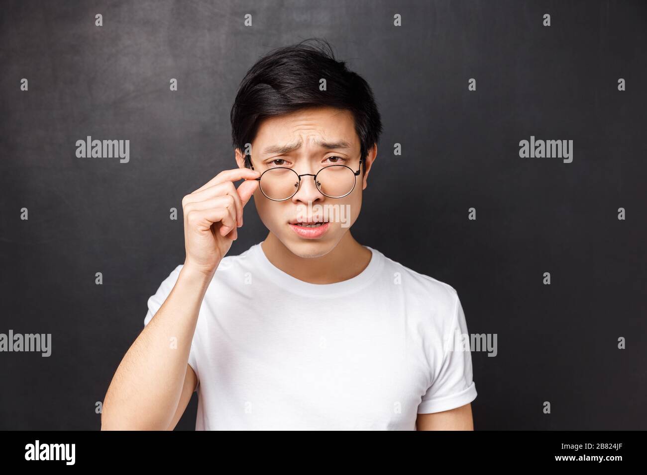 Gros plan portrait d'un homme asiatique arrogant sceptique dans un t-shirt blanc, en calant avec doute des lunettes de décollage pour regarder plus près de la personne qui parle étrange Banque D'Images