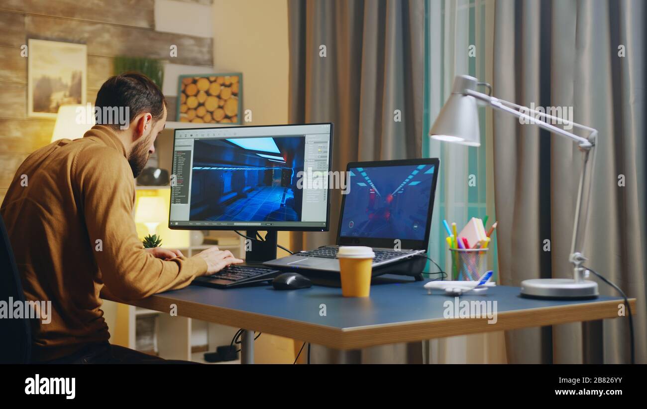 Vue arrière du jeune développeur de jeux dans son bureau à domicile travaillant sur les graphiques de l'interface. Banque D'Images