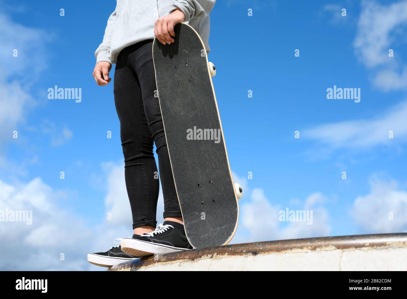 Gros plan sur un jeune homme méconnaissable tenant un skateboard dans le parc sur fond bleu ciel . Banque D'Images