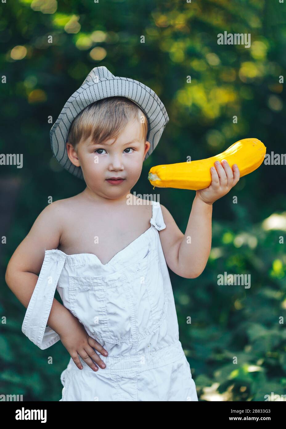 petit garçon tenant courge de courge de courge jaune dans le jardin d'été fermier garçon dans blanc décontracté robe et chapeau Banque D'Images