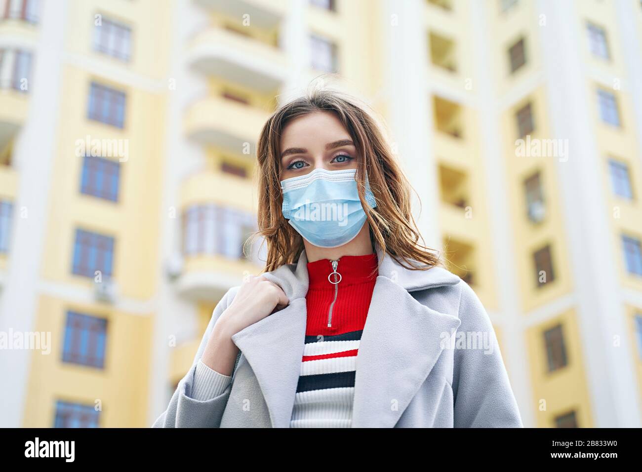 Jeune femme aux yeux bleus portant un masque de protection contre le coronavirus MERS-Cov, Novel coronavirus 2019-nCoV sur appartement jaune Banque D'Images