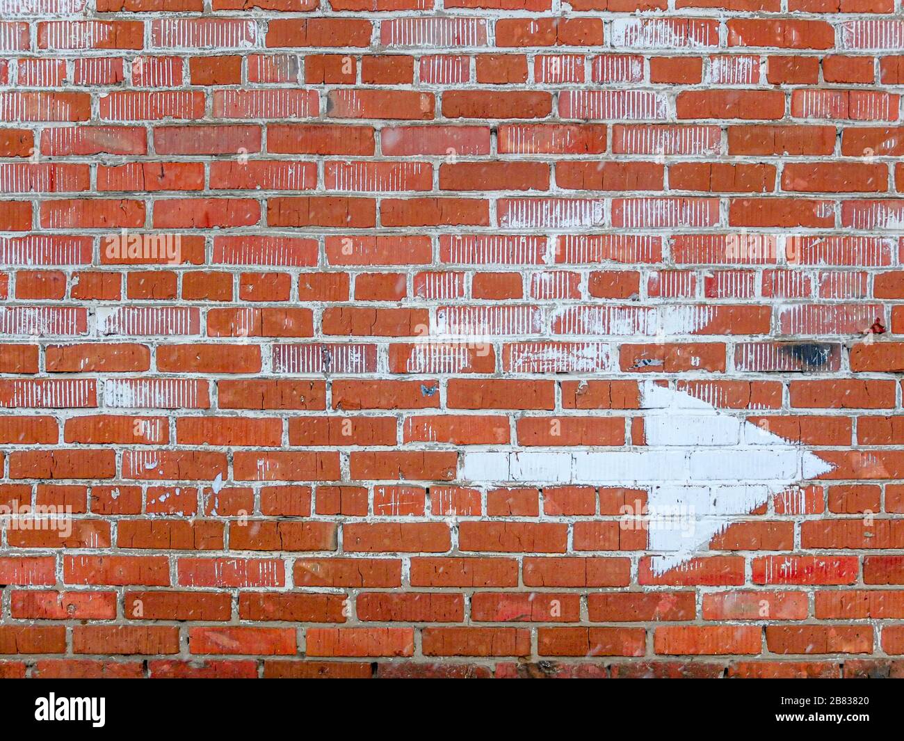 Un vieux mur de briques rouges avec des traces de peinture blanche et une grande flèche blanche dessinée pour indiquer la direction Banque D'Images