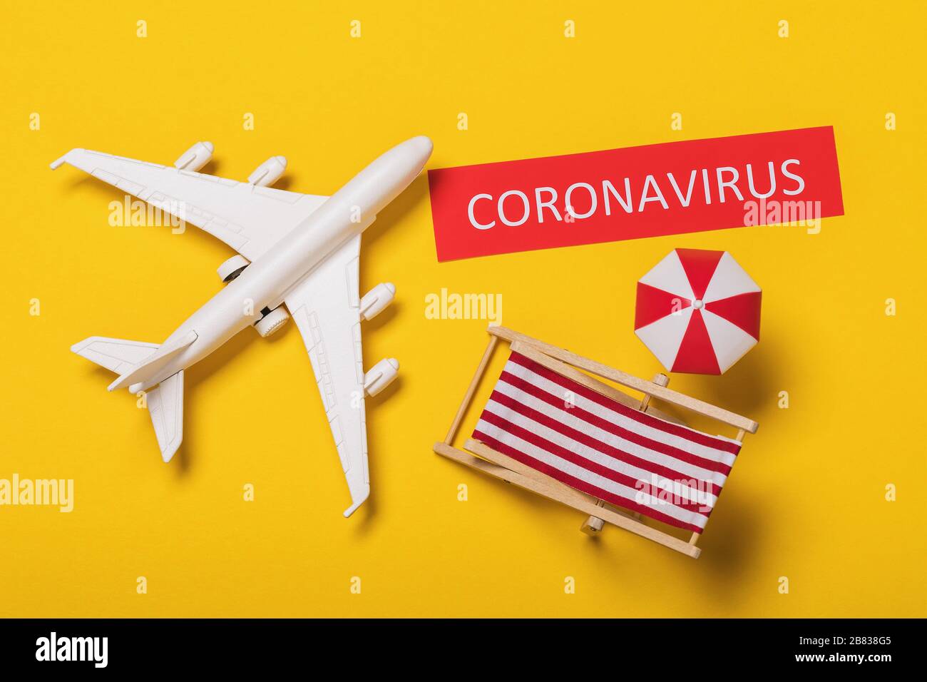 Un avion jouet, une étiquette avec une inscription et des accessoires de plage sur un fond jaune. Concept d'éclosion de coronavirus COVID-19 Banque D'Images