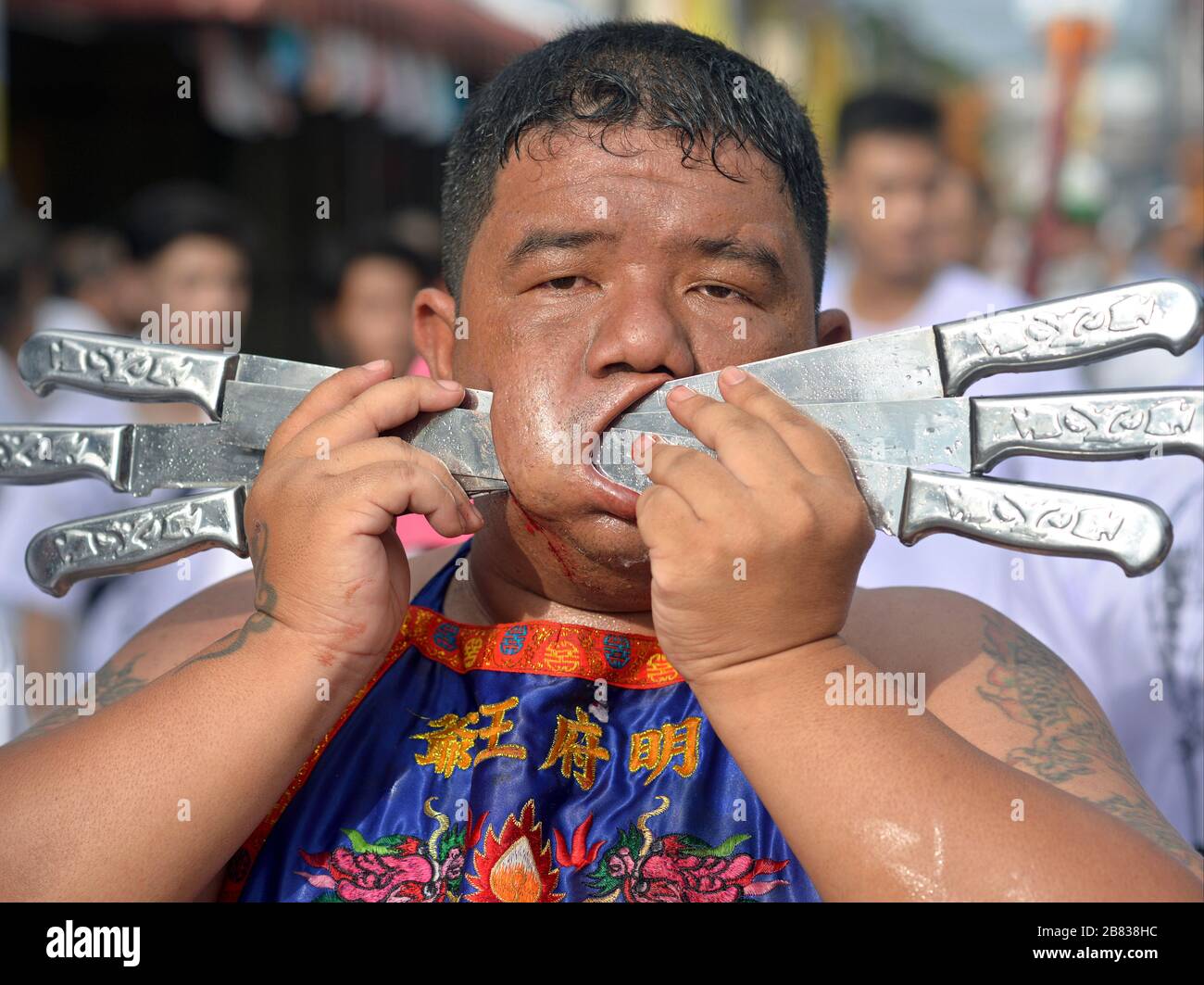 Le dévotée taoïste thaïlandais en surpoids pierces son joue droite avec six couteaux en aluminium pendant le festival végétarien de Phuket. Banque D'Images