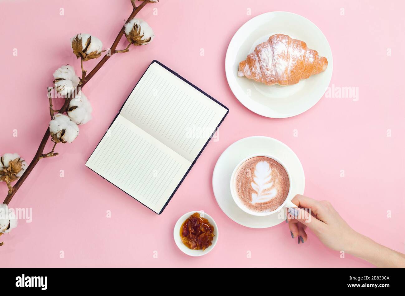 Les mains retiennent le café avec de l'art latte et un cahier avec croissant, confiture et branche en coton Banque D'Images
