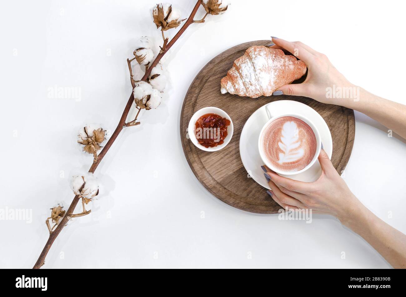 Les mains retiennent le café avec de l'art Latte avec croissant, confiture et branche en coton Banque D'Images