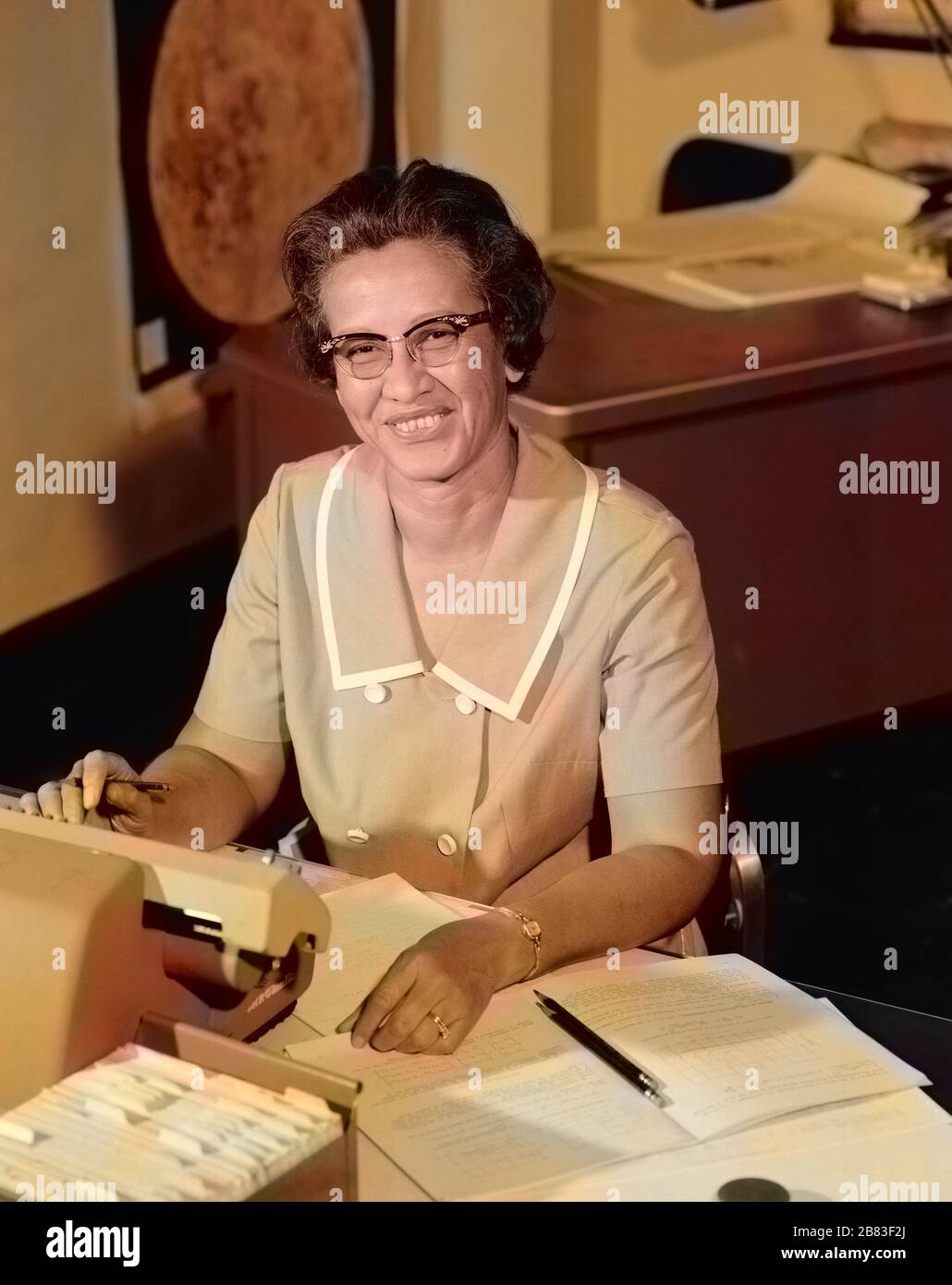 Portrait de Katherine Johnson, pionnière en informatique humaine de la NASA et en mathématiques afro-américaines (1918-2020), souriant, à un bureau avec notes, 1966. Image de courtoisie NASA. Remarque : l'image a été colorisée numériquement à l'aide d'un processus moderne. Les couleurs peuvent ne pas être précises sur une période donnée. () Banque D'Images