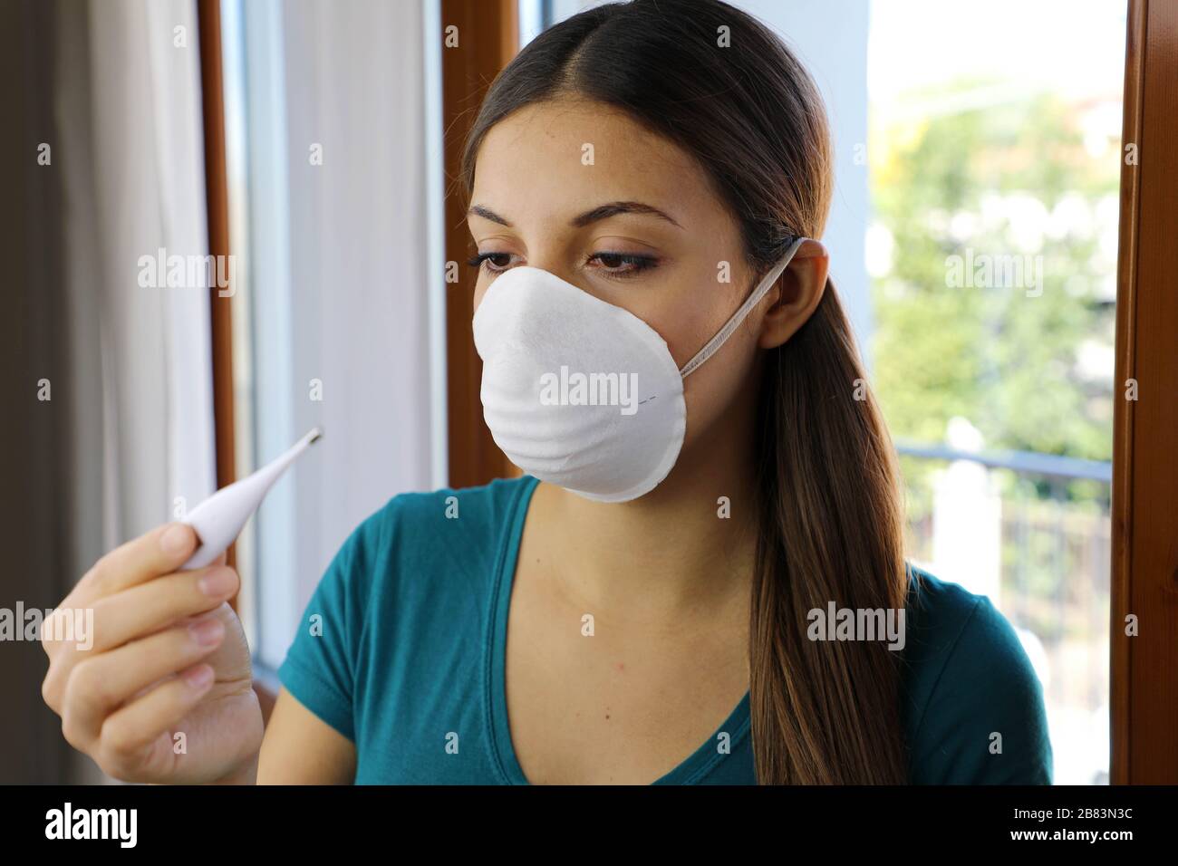 COVID-19 masque de coronavirus pandémique jamais souci Femme Vérification de la température avec thermomètre à la maison symptôme du SRAS-COV-2. Fille avec masque sur le contrôle du visage Banque D'Images