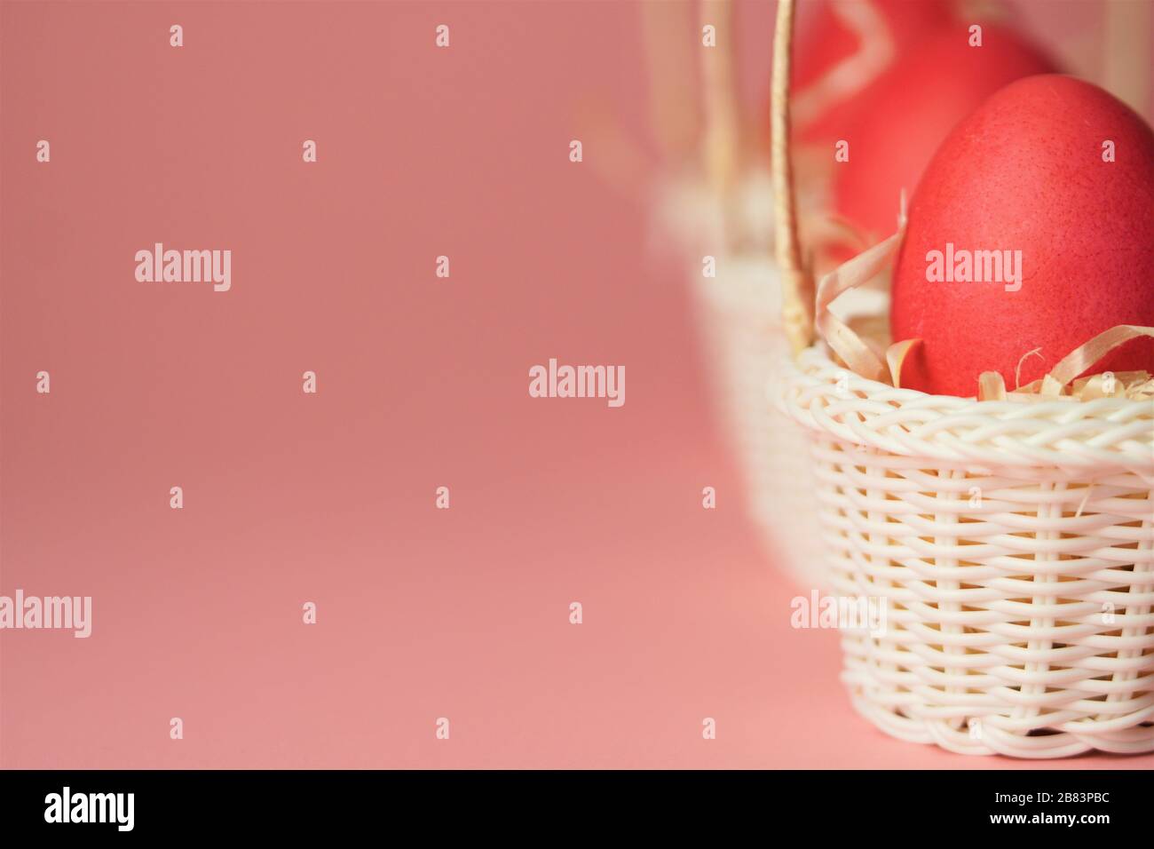 Œufs de poulet roses dans un panier en osier blanc recouvert de paille sur fond rose vif. Carte de vacances avec espace pour le texte.symbole de Pâques.espace de copie. Banque D'Images