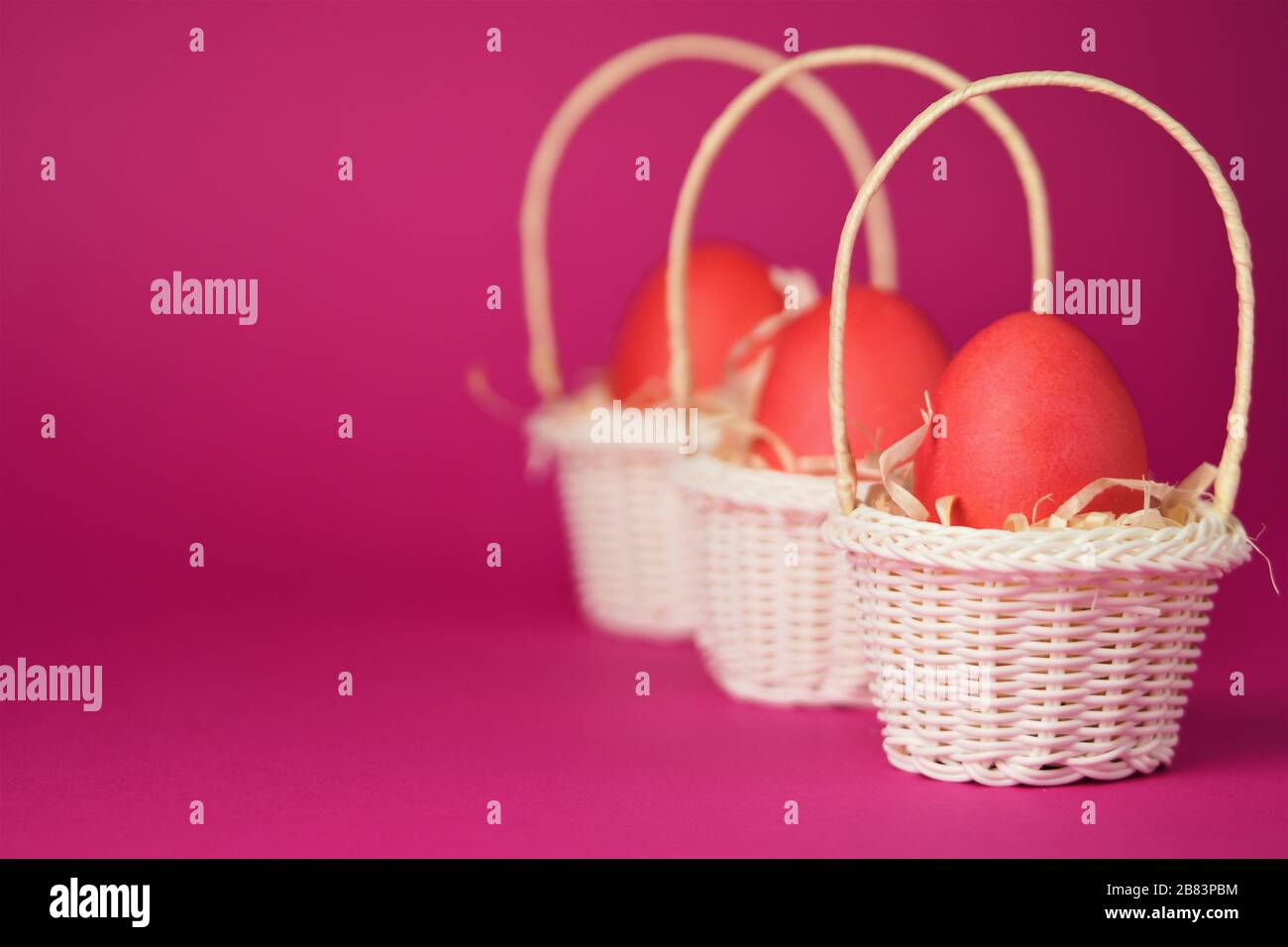 Œufs de poulet roses dans un panier en osier blanc recouvert de paille sur fond rose vif. Carte de vacances avec espace pour le texte.symbole de Pâques.espace de copie. Banque D'Images