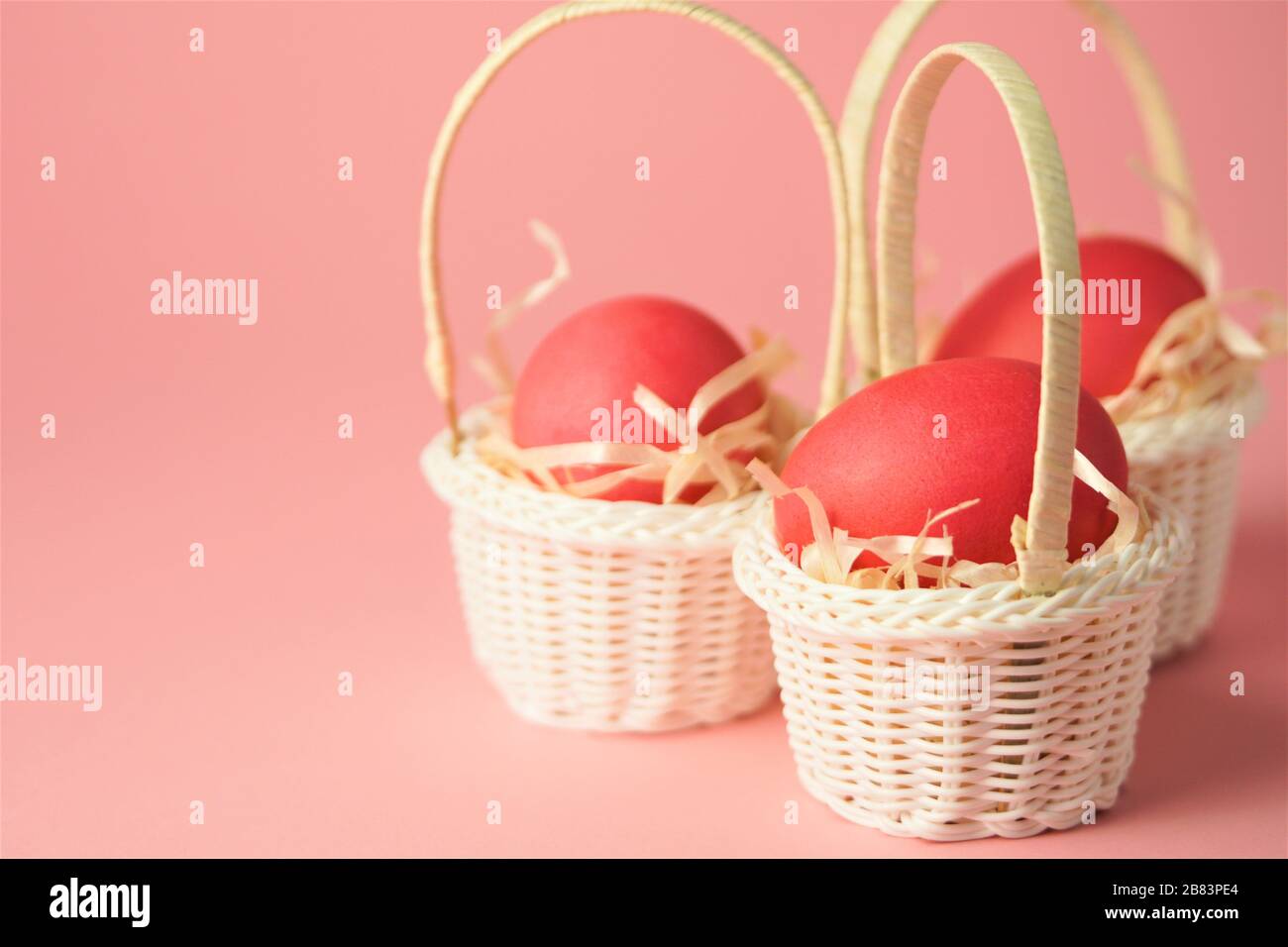 Œufs de poulet roses dans un panier en osier blanc recouvert de paille sur fond rose vif. Carte de vacances avec espace pour le texte.symbole de Pâques.espace de copie. Banque D'Images