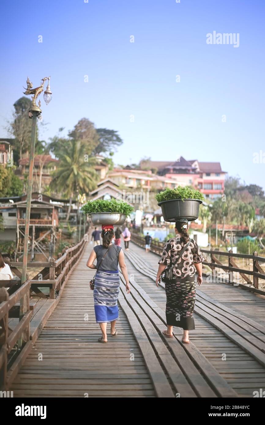 Kanchanaburi, Thaïlande - 17 janvier 2020 : les vendeurs de légumes avec bassin sur la tête marchent sur le pont Mon à Sangkhla Buri, province de Kanchanaburi Banque D'Images