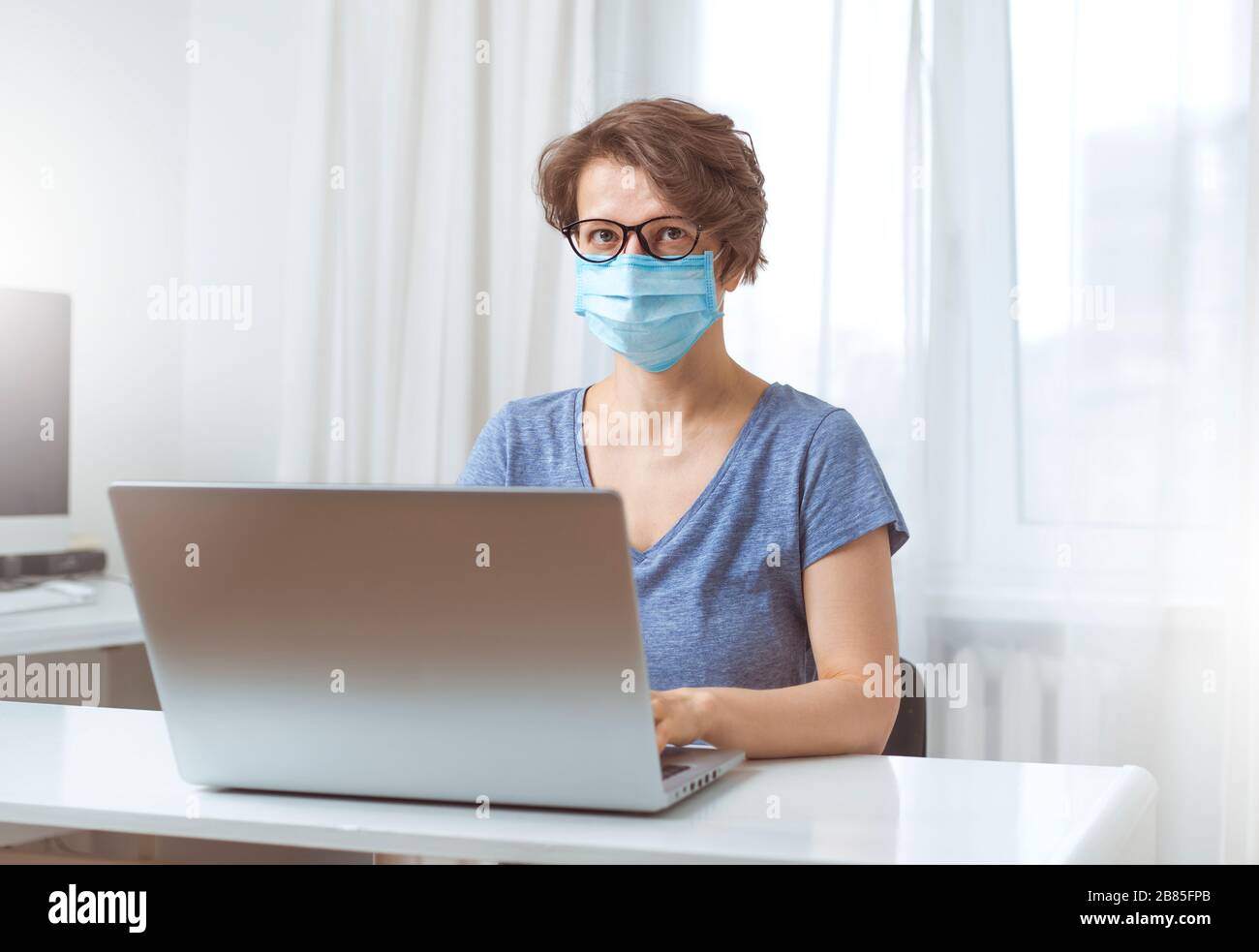 Une femme indépendante dans un masque médical travaille à distance à la maison sur un ordinateur. Le concept de quarantaine pendant les maladies virales. Banque D'Images