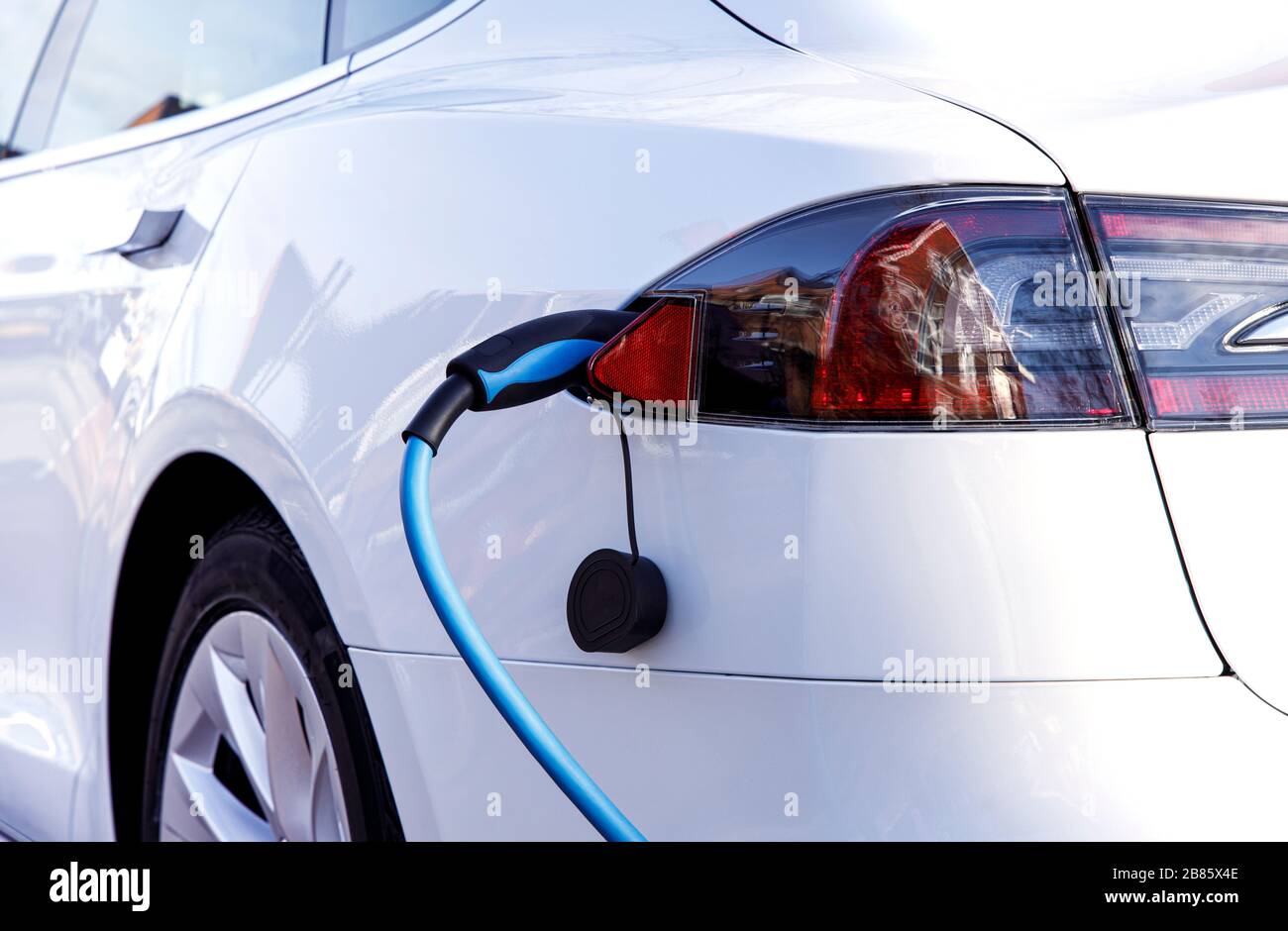 Véhicule électrique ou voiture EV blanc à la station de charge avec le câble d'alimentation branché. Concept d'énergie verte alternative écologique. Banque D'Images