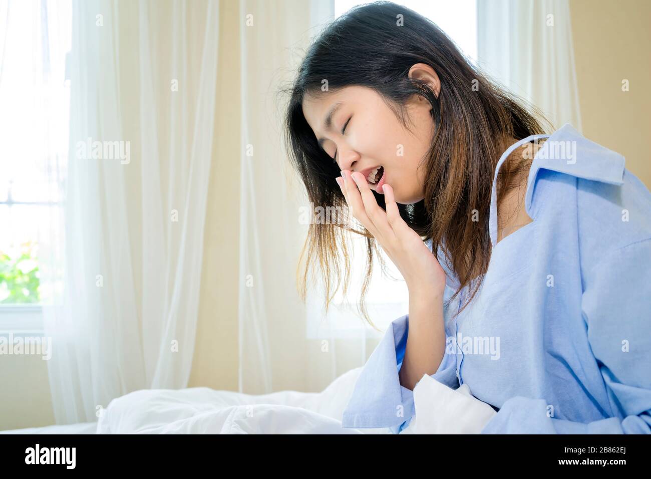 Une jeune femme endormie, épuisée, assise au lit avec des cheveux bousiches, se sentant somnolent après s'être réveillé trop tôt le matin, nuit blanche. Une adolescente fatiguée Banque D'Images