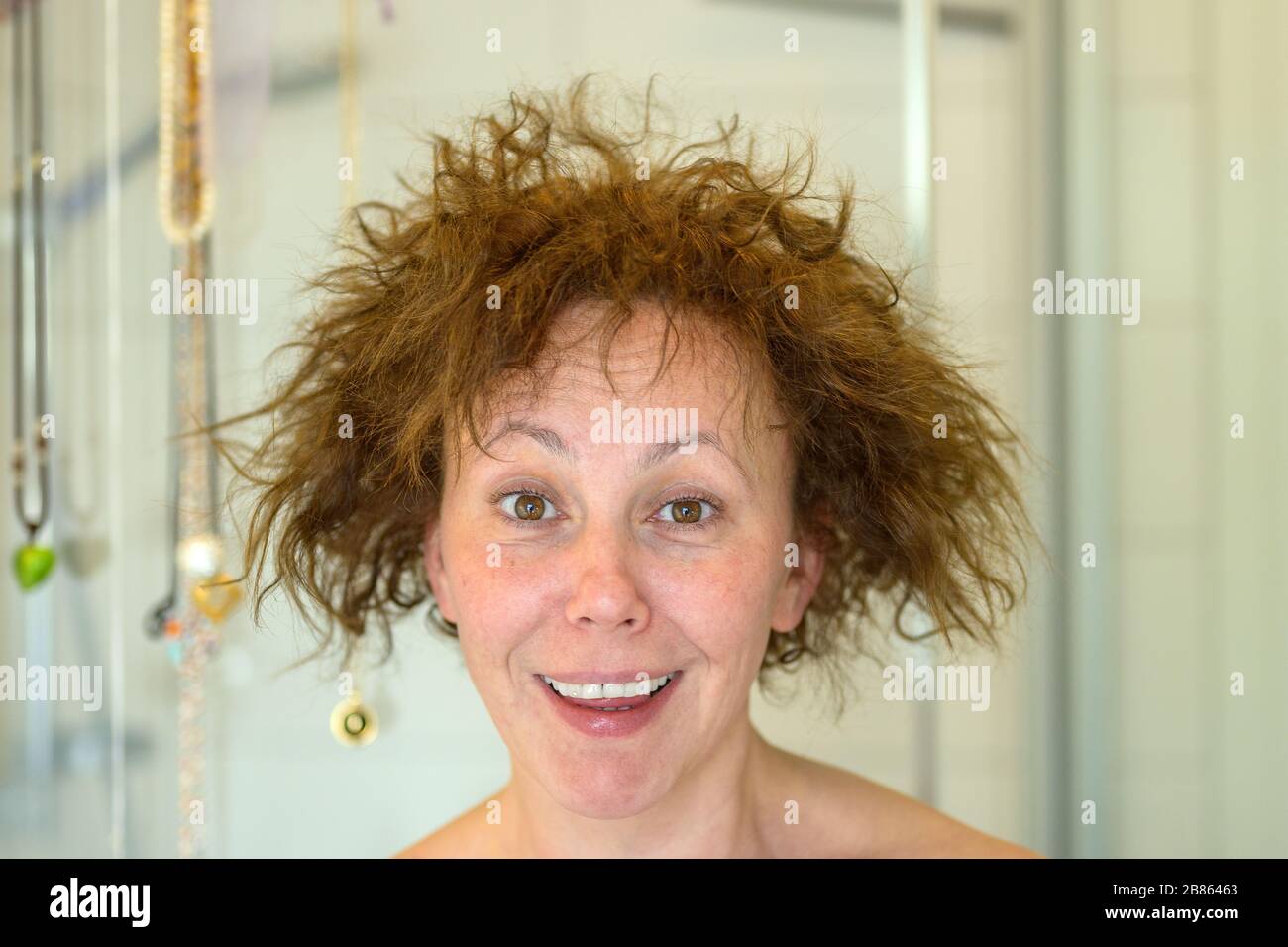 Une femme riant charismatique ayant un mauvais jour de cheveux avec ses cheveux couchés indisciplinés qui coulent dans un frizz dans un portrait de salle de bains de gros plan Banque D'Images