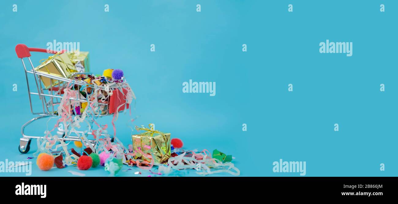 Concept Panorama. Célébrant le succès qui s'est produit, panier de supermarché placé sur un fond bleu. Il y a des boîtes-cadeaux et des rubans colorés. Banque D'Images