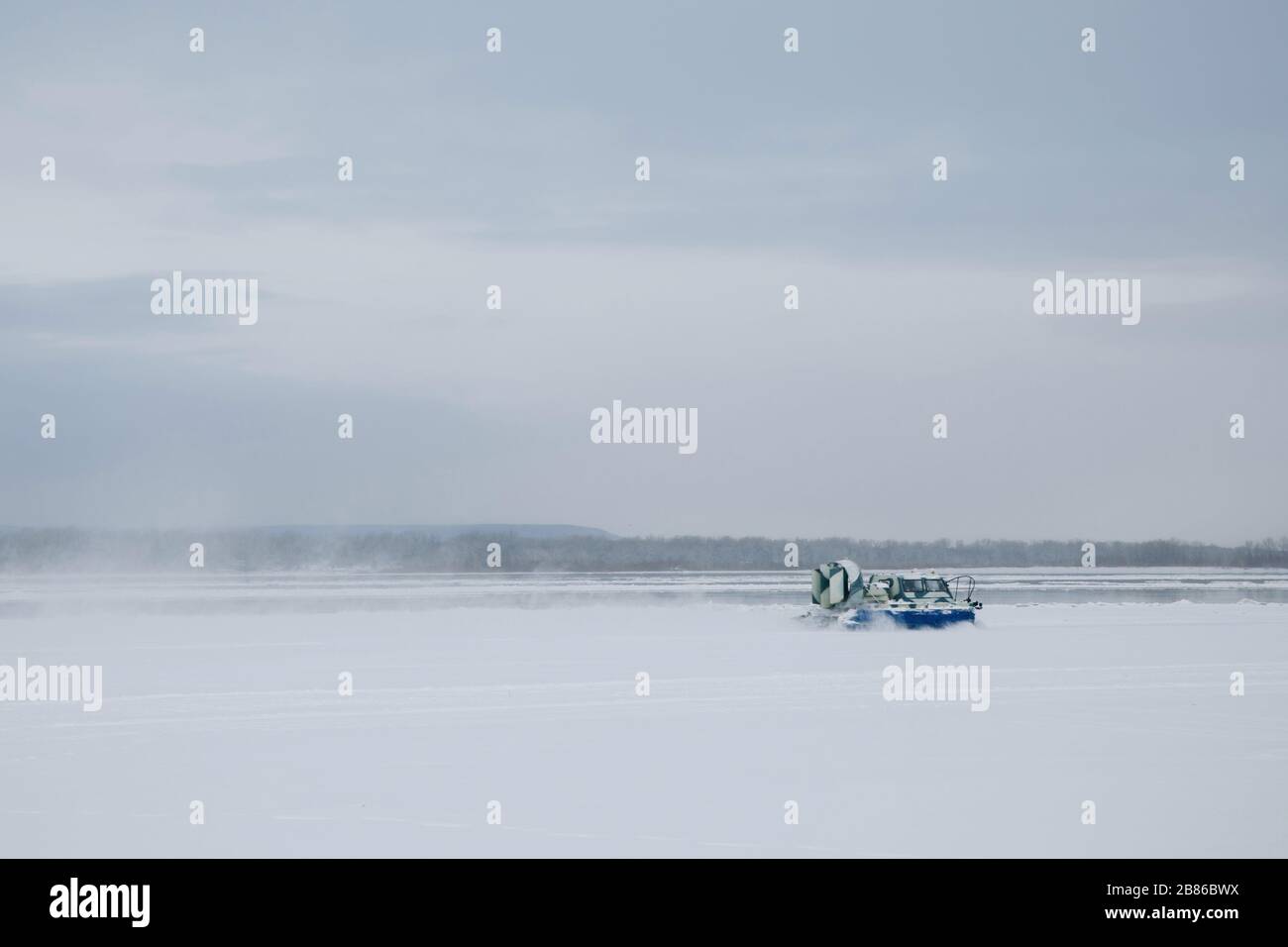 Un aéroglisseur bleu coule le long de la rivière Volga enneigée. Un blizzard de neige s'élève sur elle. Banque D'Images