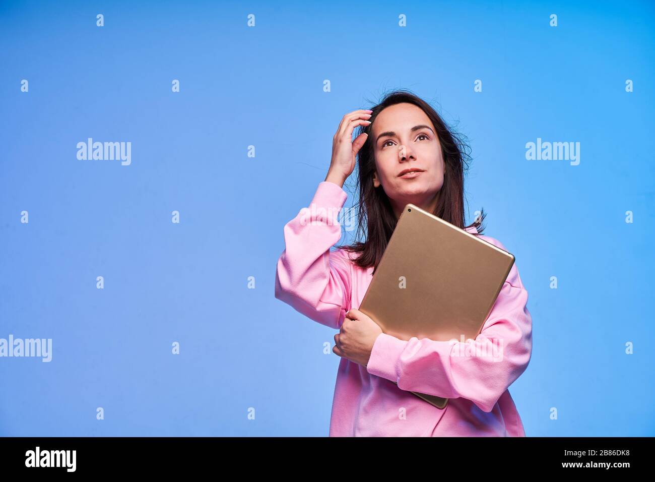 Jeune femme belle avec tablette regardant le haut sur fond bleu Banque D'Images