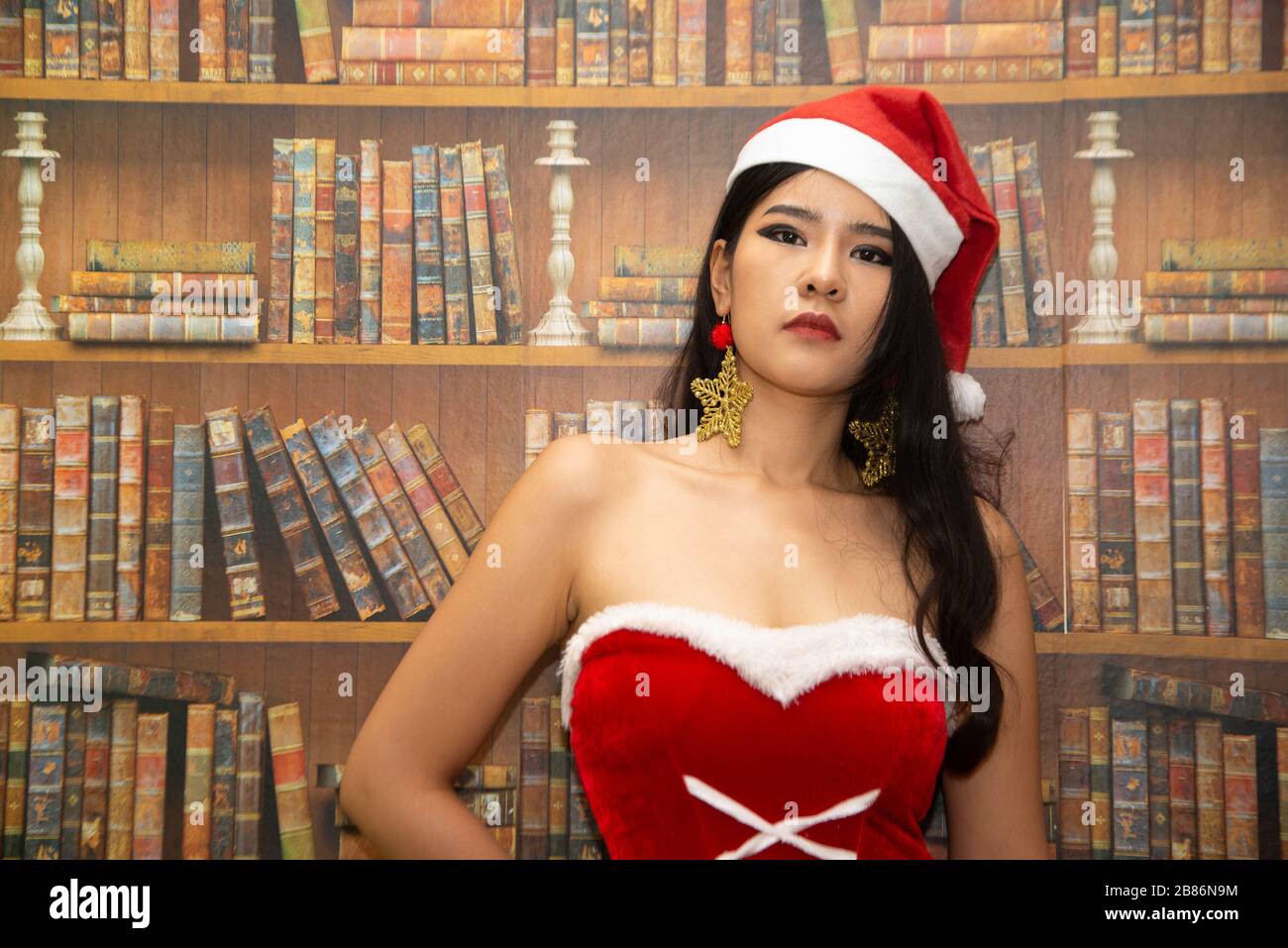 Une belle femme asiatique vêtue d'une tenue de Santa montre un style différent. Avec l'arrière-plan de la bibliothèque comme concept pour le jour de Noël. Banque D'Images