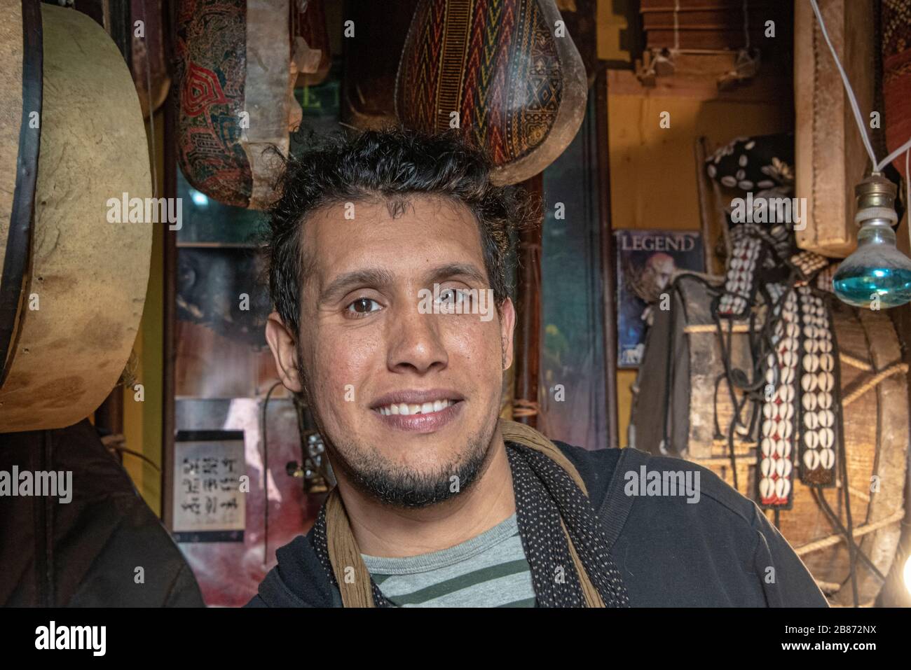 Essaouria, Maroc - septembre 2017 : Portrait lumière naturelle d'un homme marocain, mi-30, debout dans un magasin entouré d'instruments Banque D'Images