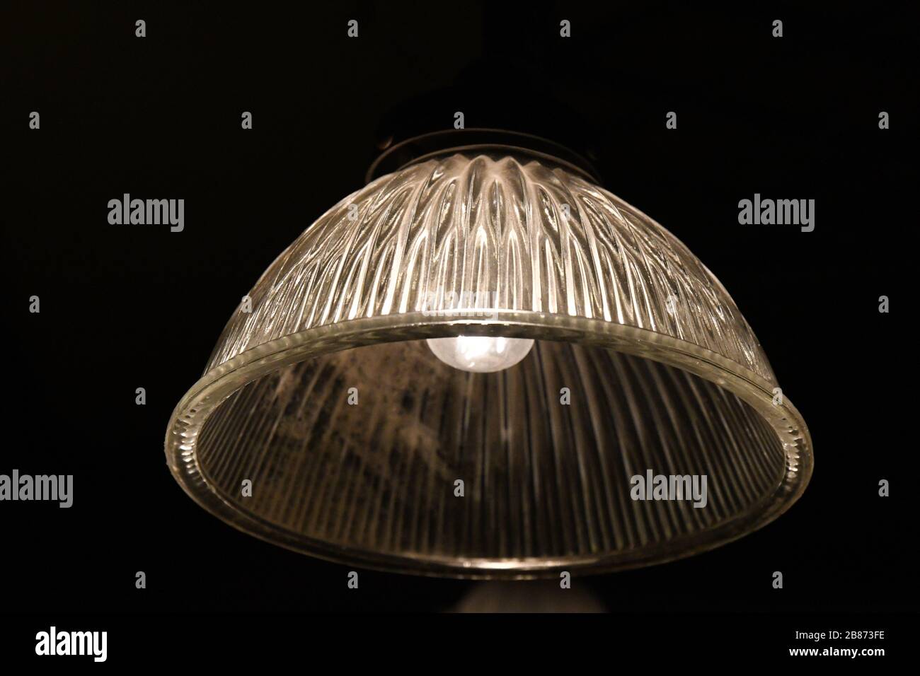 Lampadaire en verre orné de style vintage se ferme sur fond noir. Surface striée de la lampe en verre transparente avec ampoule à l'intérieur. Suspension ancienne Banque D'Images