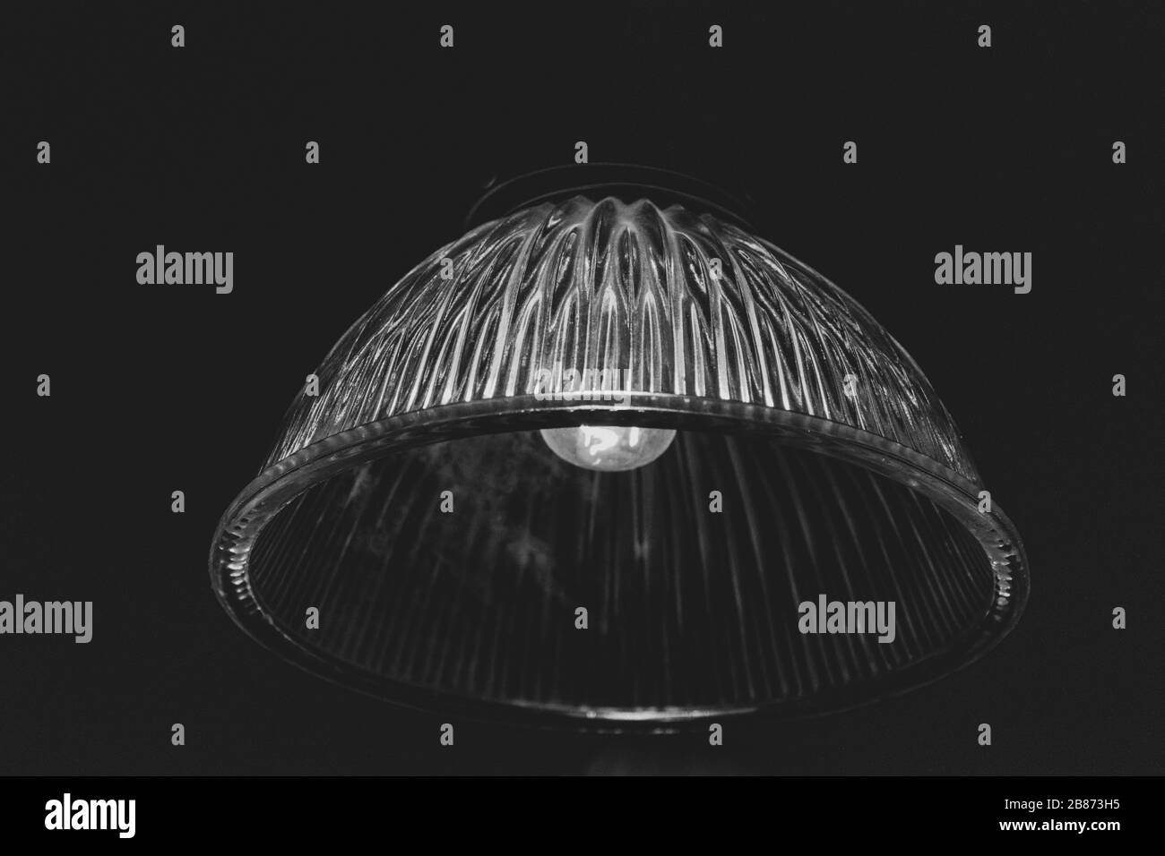 Photographie en noir et blanc de la lampadaire de verre orné d'époque se rapprochez sur fond noir. Surface striée de la lampe en verre transparente avec ampoule Banque D'Images