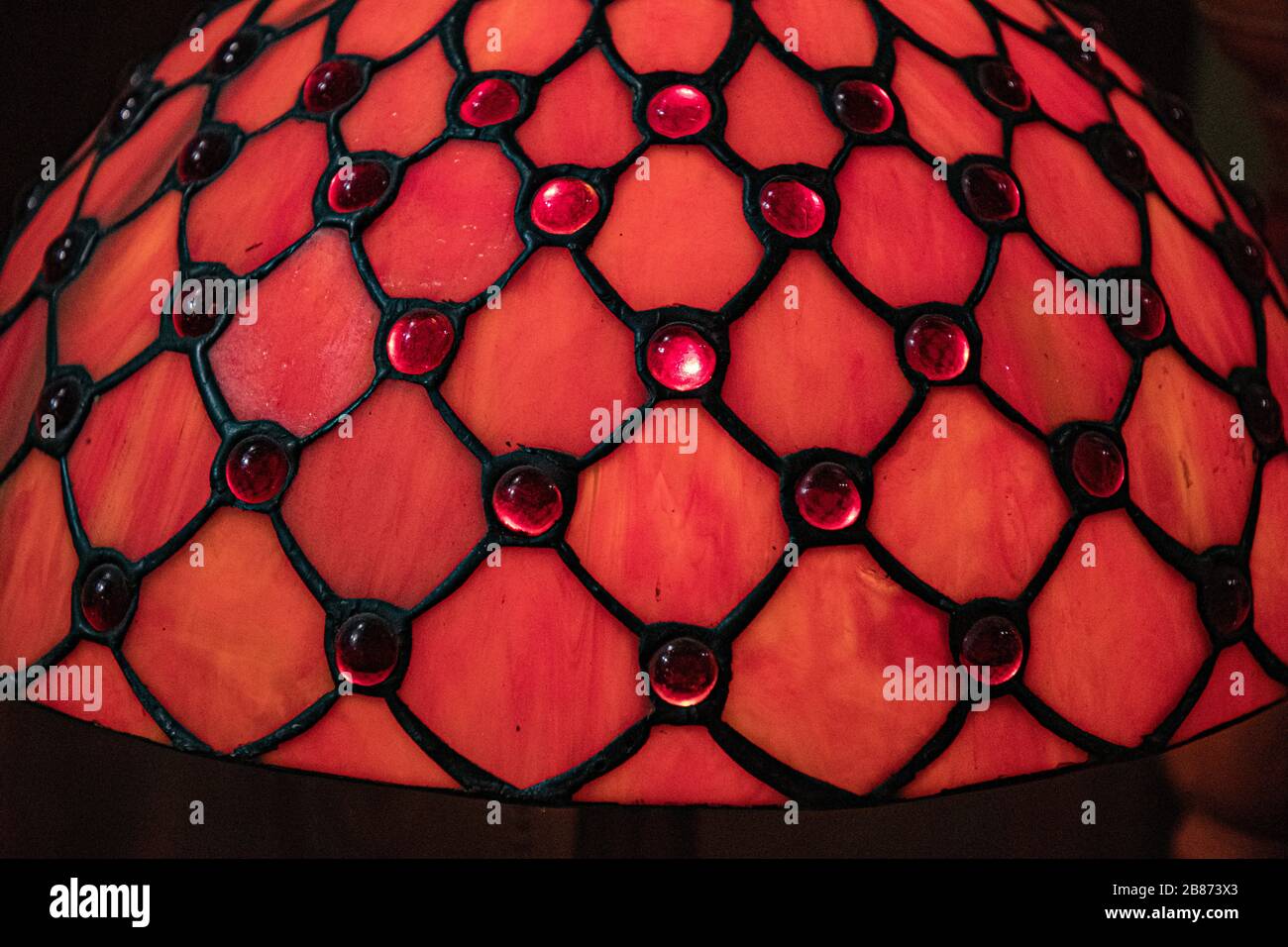 Surface en vitrail rouge brillant avec motif losange noir et pierres en verre étincelant. Structure mate de lampadaire en verre ancien de la table vintage Banque D'Images