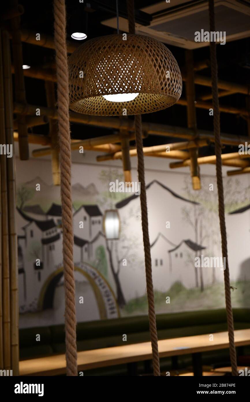 Décoration intérieure chinoise traditionnelle en cordes et ficelles. Ombre de lampadaire en osier suspendue et fond peint ethnique flou. Intérieur en bois. Banque D'Images
