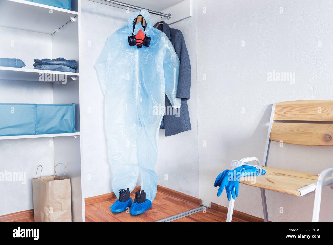 combinaison de protection contre le coronavirus accrochée dans une armoire à la maison avec couvre-chaussures bleus, gants bleus, masque rouge et lunettes transparentes Banque D'Images