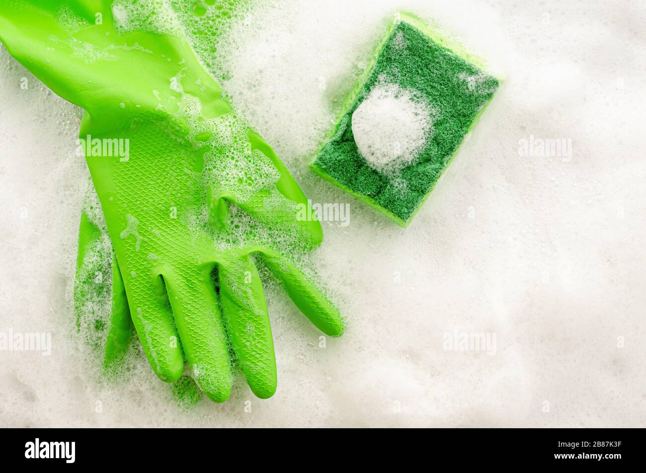 Vue de dessus des gants de protection verts et de l'éponge sur fond savonneux. Concept de travaux ménagers. Espace de copie, vue de dessus Banque D'Images