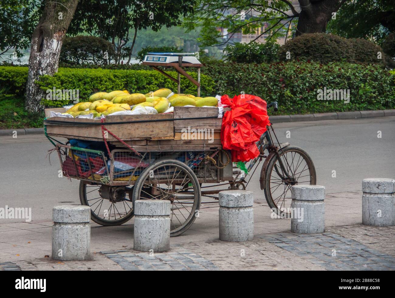 Guilin, Chine - 10 mai 2010: Centre-ville. Vélo à pédale de tricycle ancien avec compartiment de chargement en bois plein de papayas mûrs vert-jaune dans la rue de surface grise. Banque D'Images