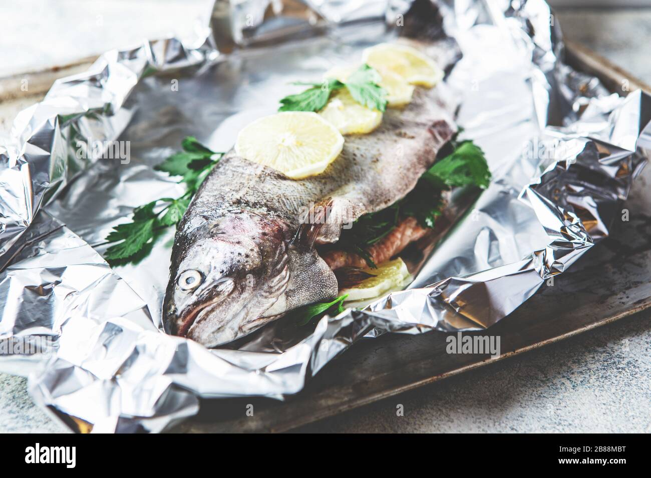 Truite arc-en-ciel fraîche avec persil et citron en feuille d'aluminium sur fond gris clair. Des aliments sains. Concept de cuisson. Banque D'Images