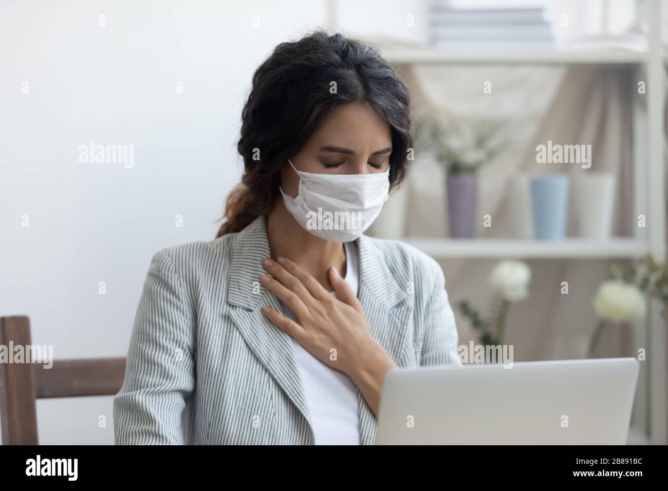 La femme d'affaires dans le masque assis sur le bureau de travail se sent malsaine Banque D'Images