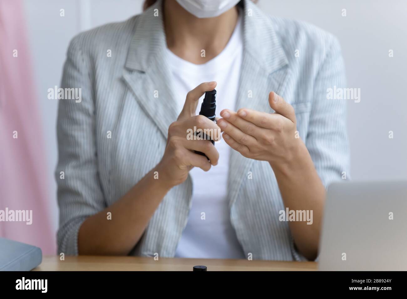 La femme dans le masque nettoie les mains en vaporisateur de solution désinfectante Banque D'Images