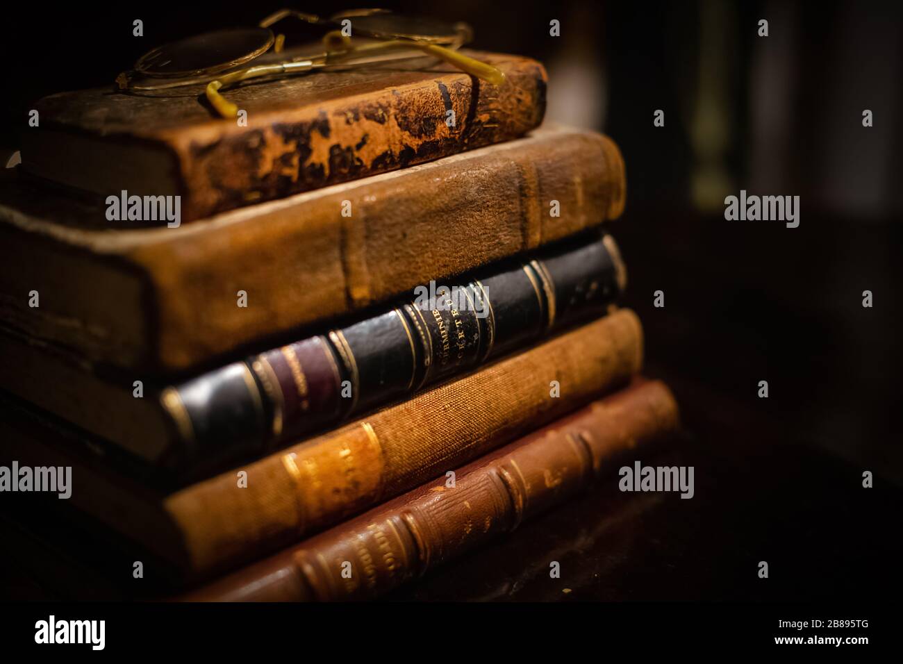 Une pile vintage de trois vieux livres en cuir brun avec des lunettes de vue sur une table en bois. Banque D'Images