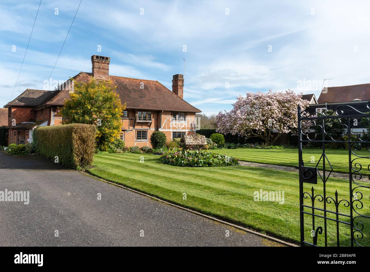 Grande maison avec pelouse, arbre magnolia et portes métalliques décoratives dans le village West Sussex d'Itchenor, Royaume-Uni Banque D'Images