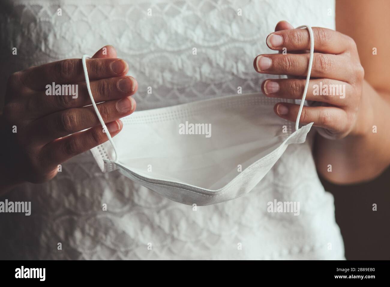 Les mains de la mariée tenant le masque médical blanc. Femme en robe de mariage pendant l'épidémie de Coronavirus. Mariages annulés ou différés causés par l'éclosion de COVID-19. Concept de coronavirus, photo conceptuelle. Banque D'Images