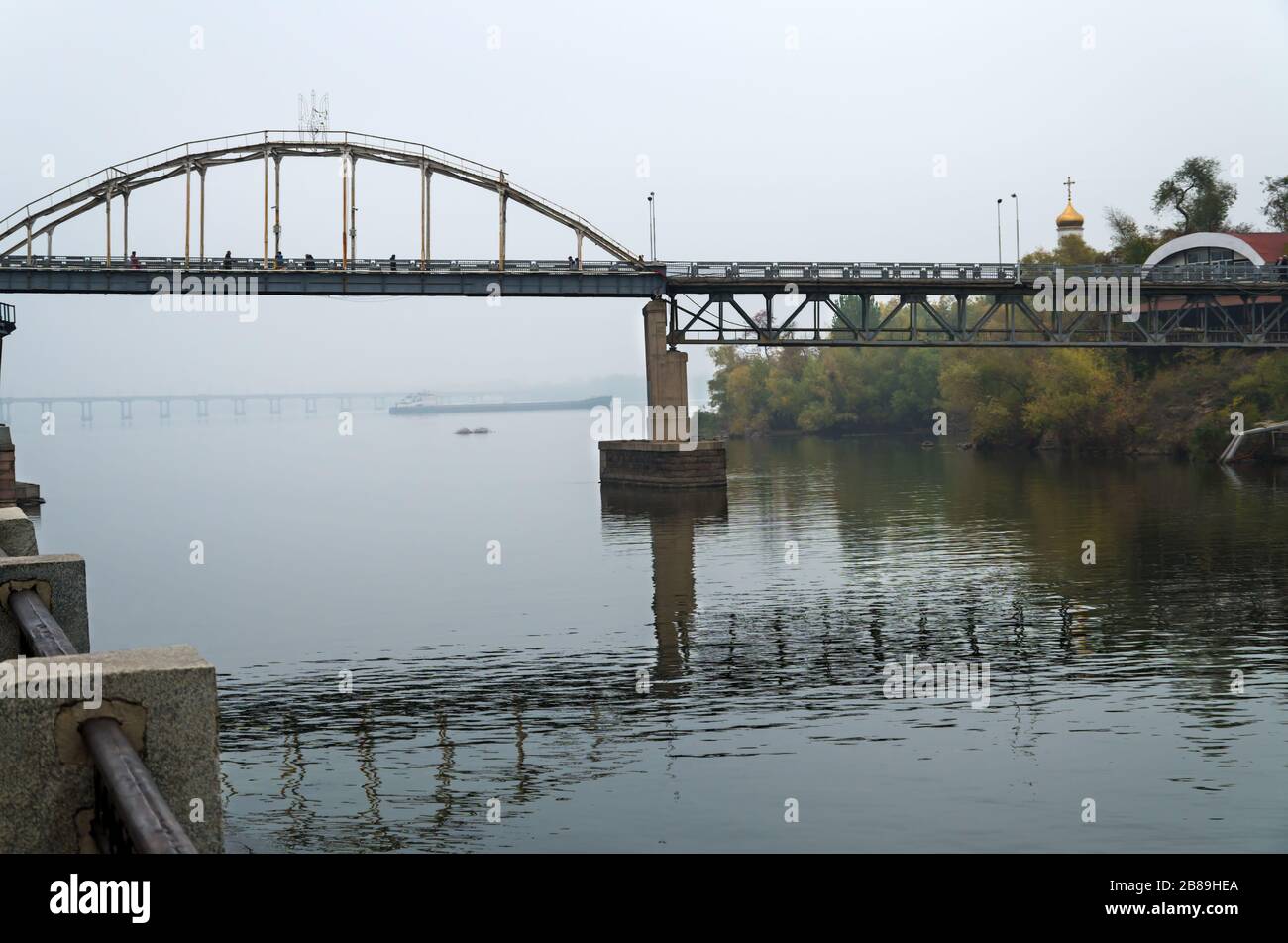 Pont de pied en métal dans le brouillard d'automne sur le fond duquel flotte le bateau de rivière Banque D'Images