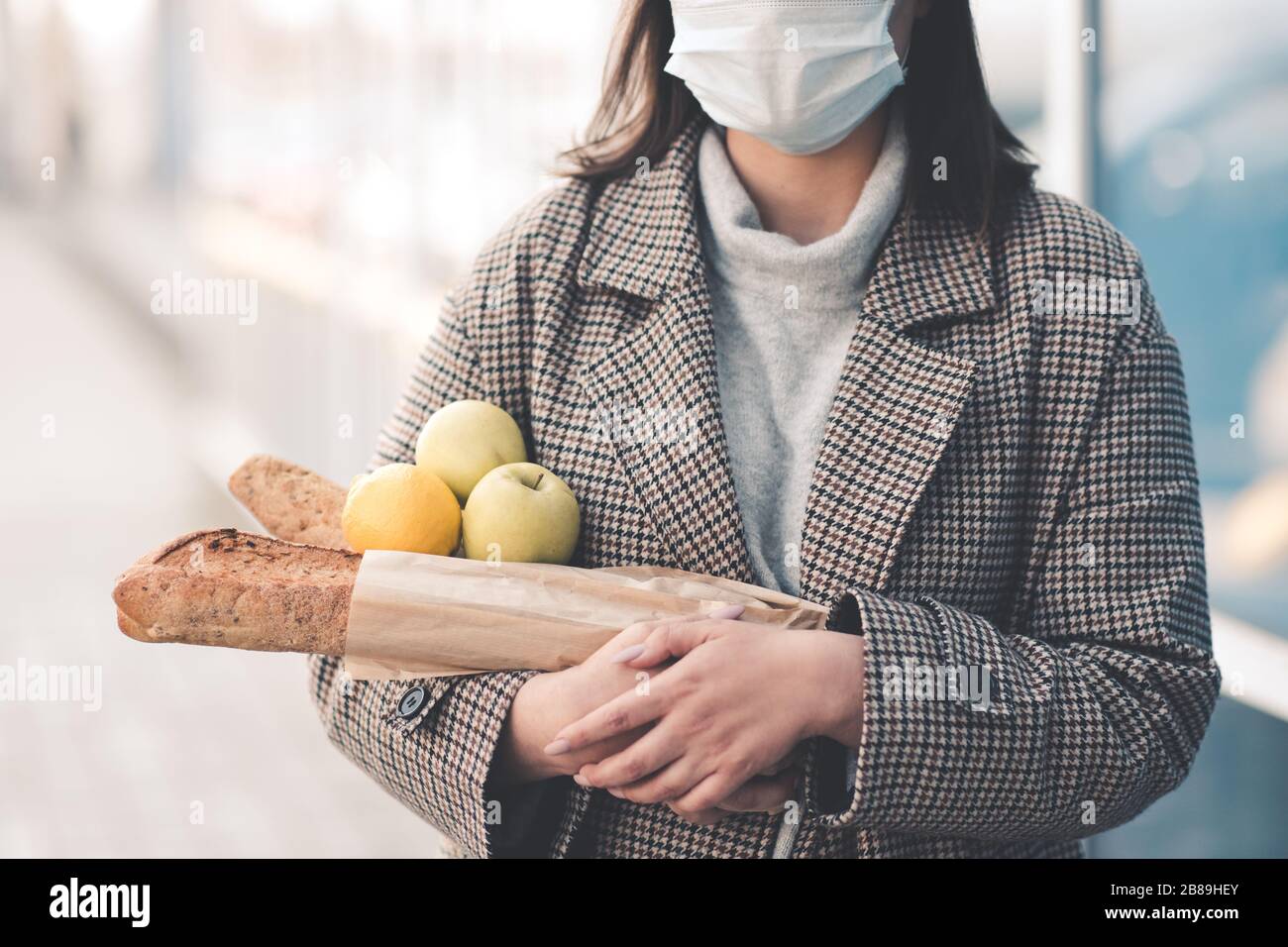 Jeune femme tenant des aliments marchant dans la rue portant un masque médical à l'extérieur. Distanciation sociale. Concept de virus. Banque D'Images
