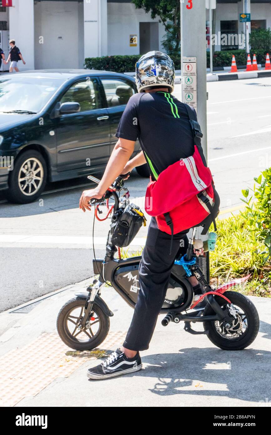 Singapour - 8 juillet 2019: Homme sur un petit vélo attendant de traverser un passage piéton. De nombreuses personnes utilisent cette forme de transport Banque D'Images