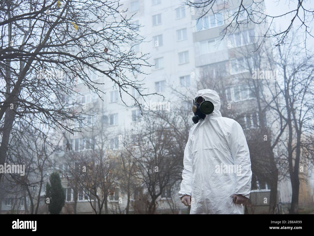Vue latérale de l'écologiste en uniforme de protection debout sur la rue moggy et regardant de côté. Homme écologiste portant un costume blanc et un masque à gaz. Concept d'écologie et de pollution environnementale. Banque D'Images