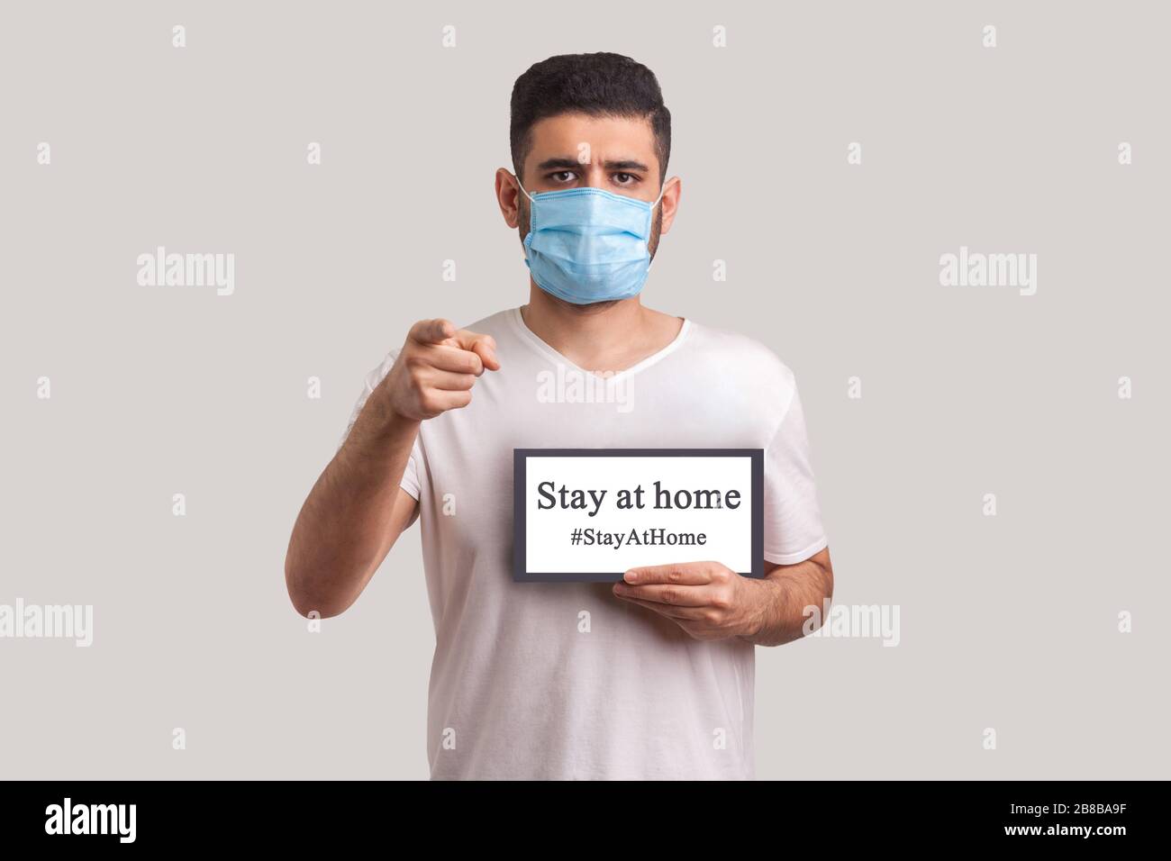 #StayAtHome. Homme dans un masque de protection tenant rester à la maison inscription et pointant vers la caméra, avertissement de quarantaine du coronavirus, épidémie de Covid-19, pré Banque D'Images